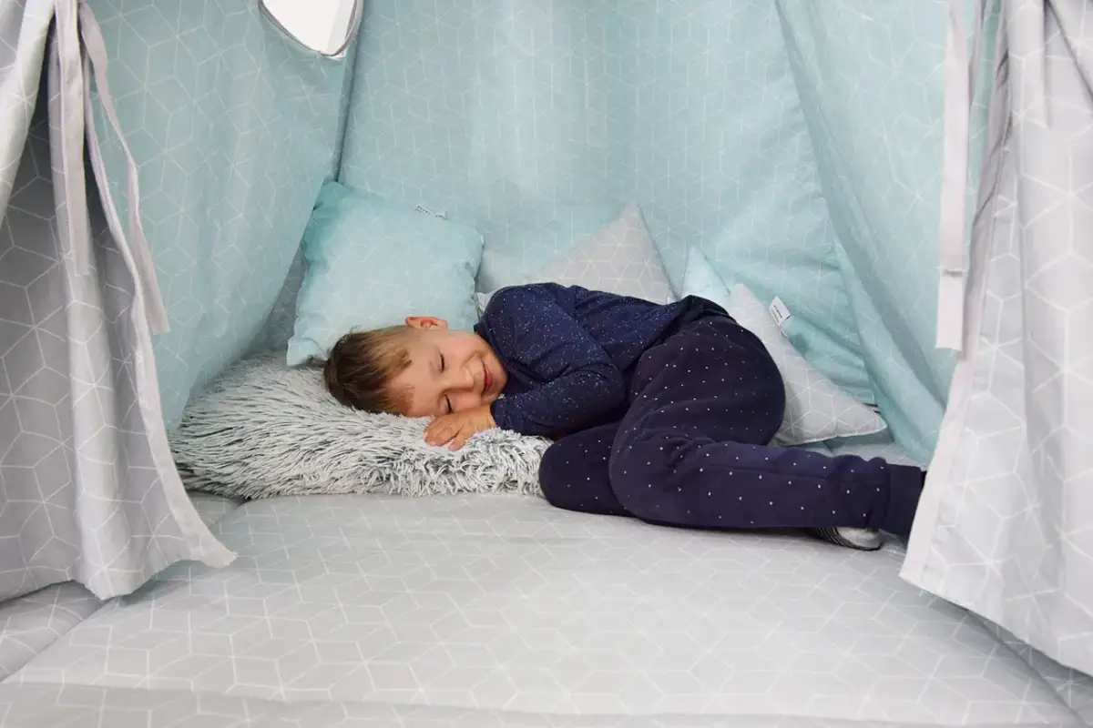 Chłopiec śpi w domowej bazie z poduszkami. Idealne miejsce, by odpocząć po zabawie.