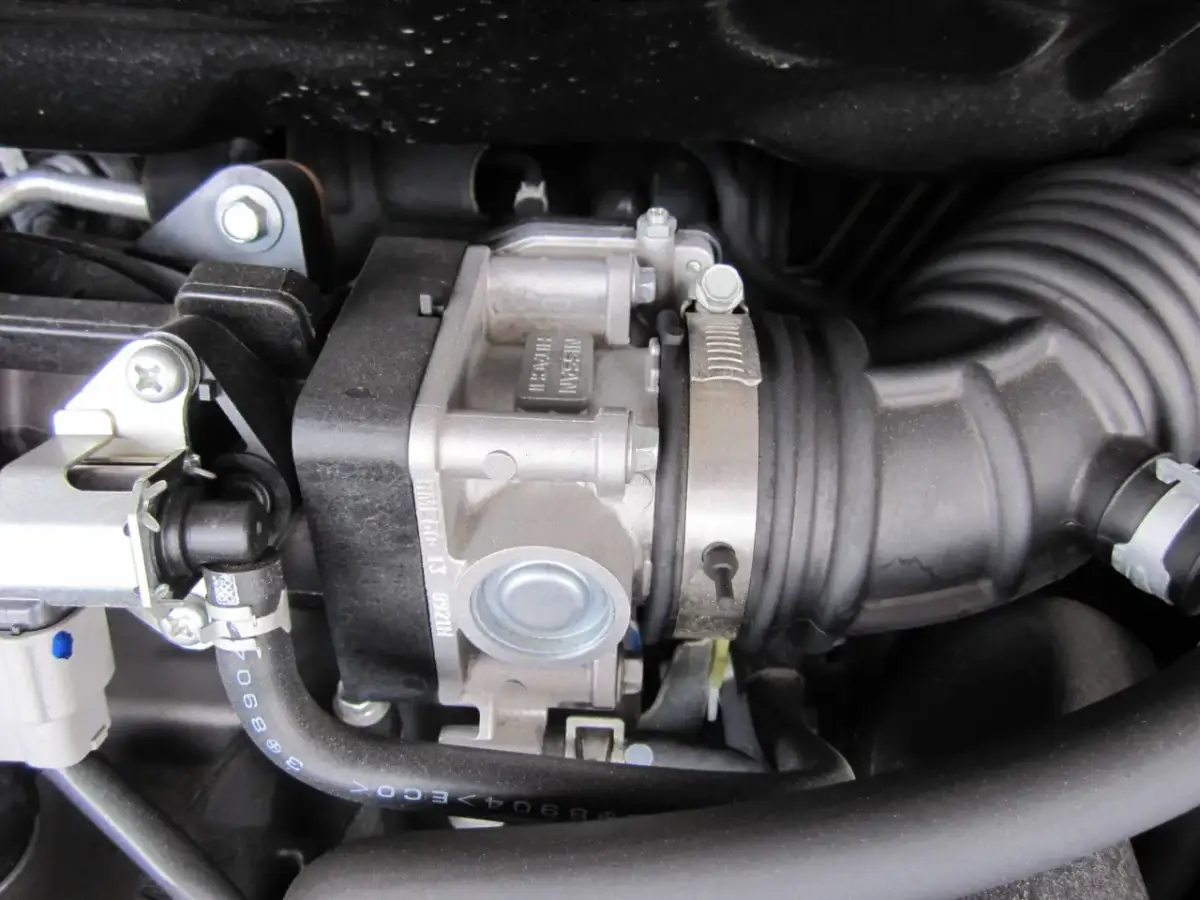 Widok na przepustnicę silnika Nissana, gdzie jest zamontowana w układzie dolotowym, otoczona przewodami i elementami silnika.