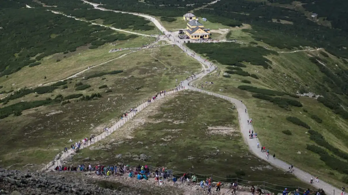 Tłum turystów podąża szlakiem na Śnieżkę, wspinając się po kamienistym zboczu.