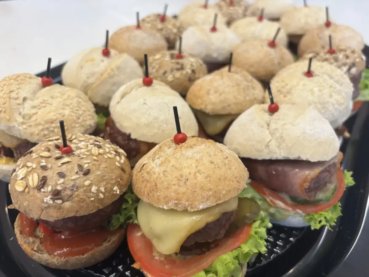 Mini hamburgery gdzie kupić? Taca pełna pysznych, małych burgerów z serem, warzywami i różnymi bułkami. Idealne na imprezę!