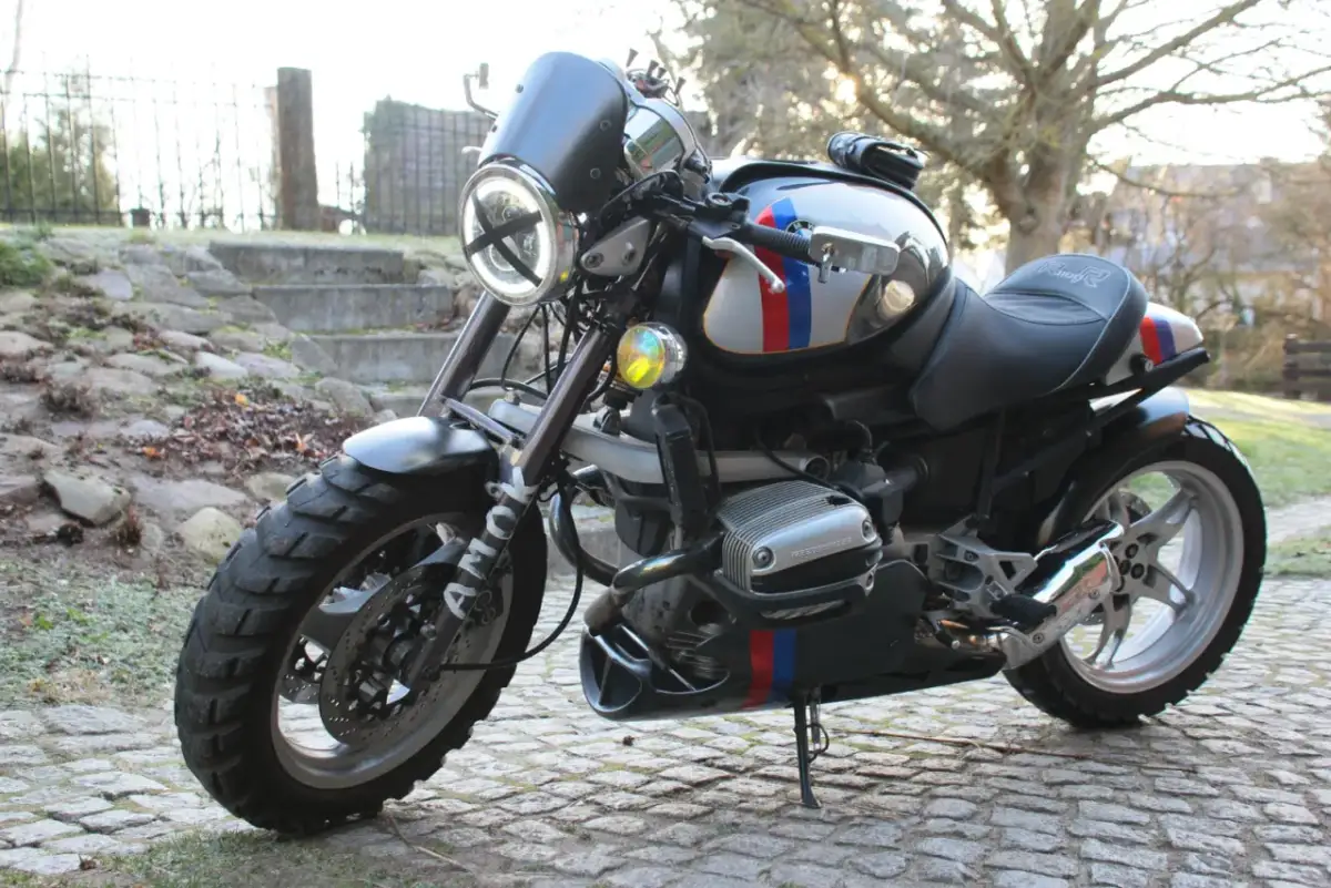 Zmodyfikowany BMW R 1100 R z okrągłym reflektorem i ozdobnymi pasami w barwach narodowych, gotowy na przygodę.