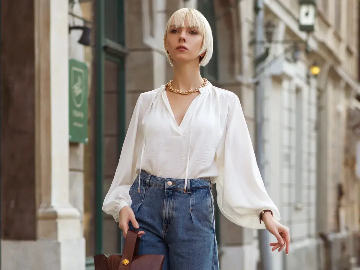 Elegancka biała bluzka z bufiastymi rękawami i jeansowe, szerokie spodnie. Idealna stylizacja, która odpowiada na pytanie: jaka bluzka do szerokich spodni.