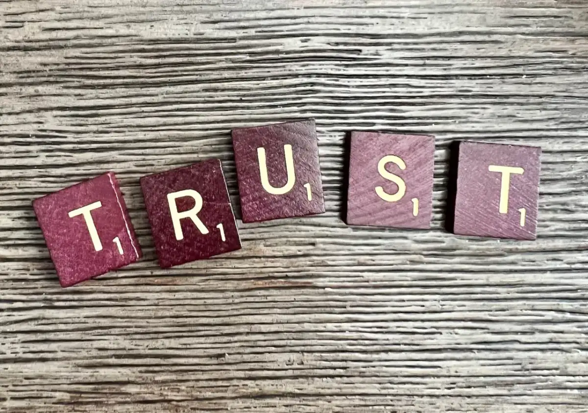 Litery "TRUST" ułożone na drewnianym tle. Brak zaufania w związku czy to ma sens?