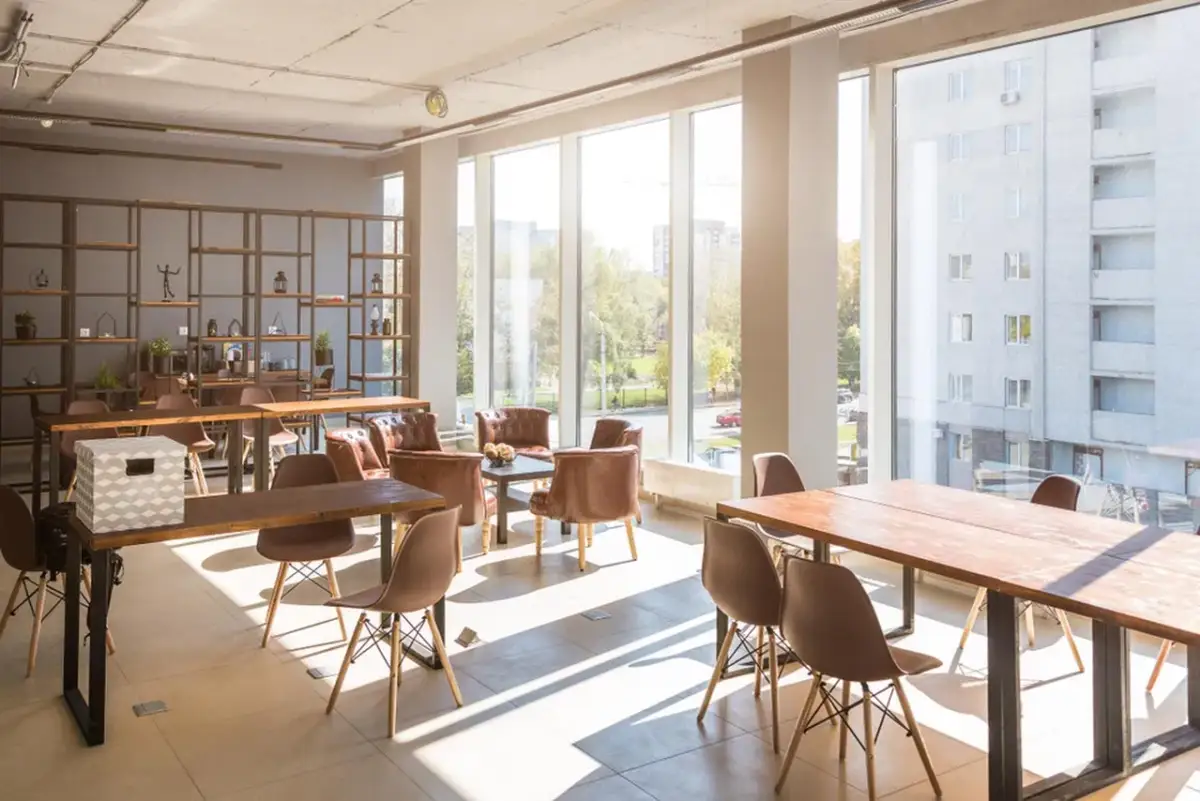 Jasne, nowoczesne wnętrze z dużymi oknami, stołami i krzesłami. Idealne miejsce na coworking, które może być świetnym lokalem inwestycyjnym.