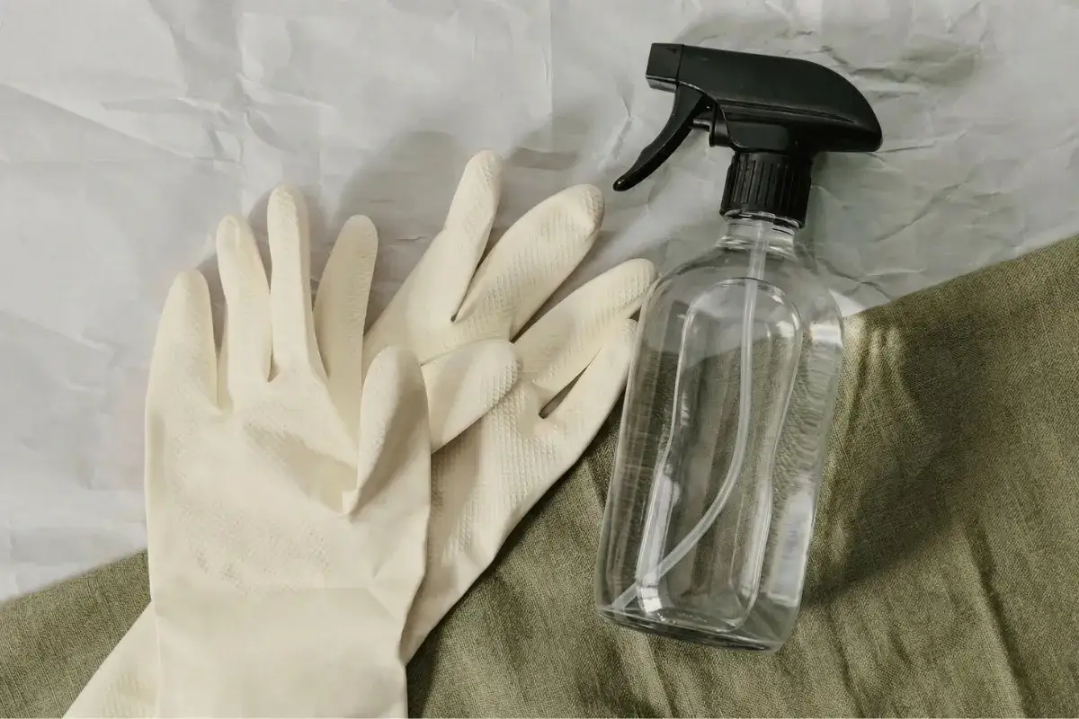 Para gumowych rękawiczek i butelka z atomizerem na zielonym tle.