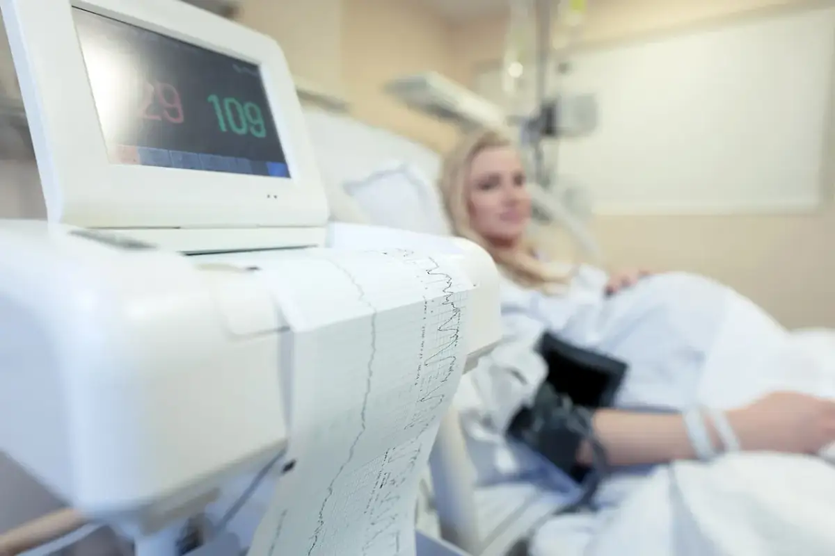 Monitor KTG z wydrukiem zapisu i ciężarną w tle.