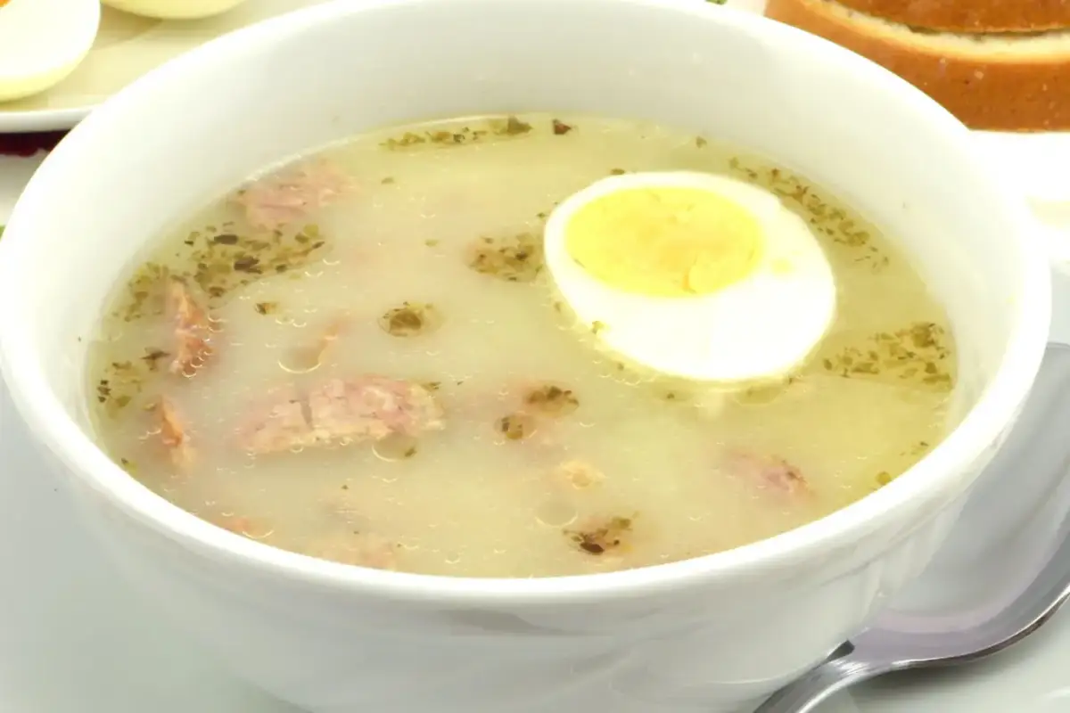 Biała miska z zupą, w której widać kawałki kiełbasy i połówkę jajka na twardo.