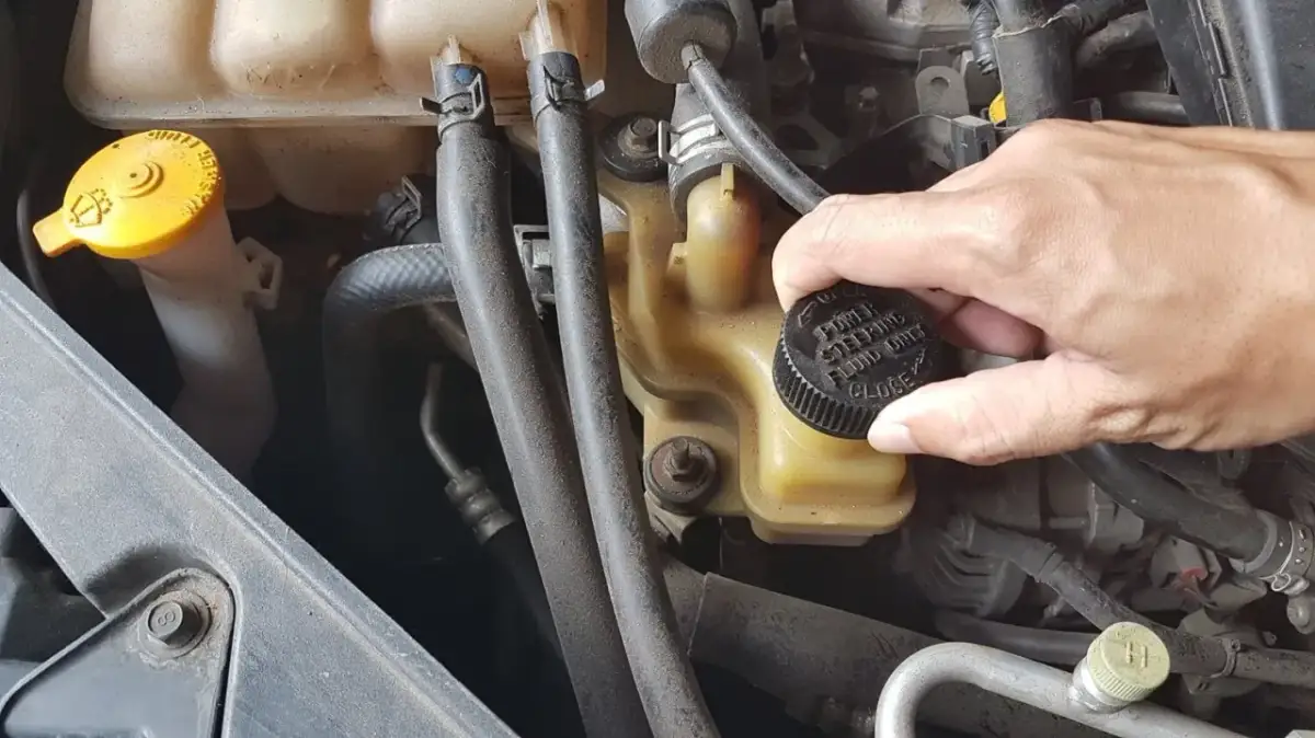 Dłoń odkręca czarną nakrętkę z napisem "POWER STEERING FLUID ONLY". To zbiorniczek, gdzie wlać płyn do wspomagania kierownicy.