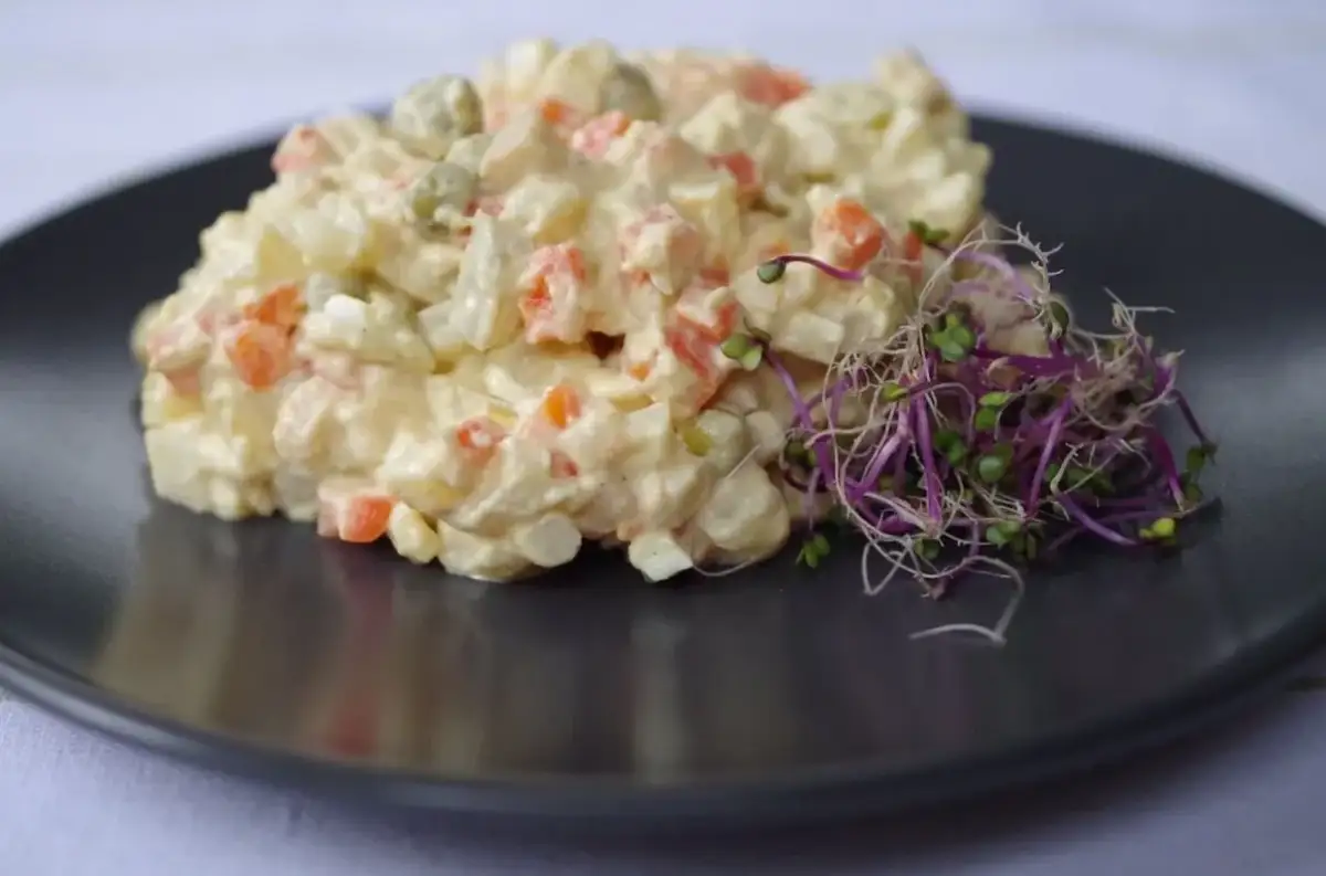 Sałatka jarzynowa z groszkiem, marchewką i jajkiem, udekorowana kiełkami rzodkiewki.