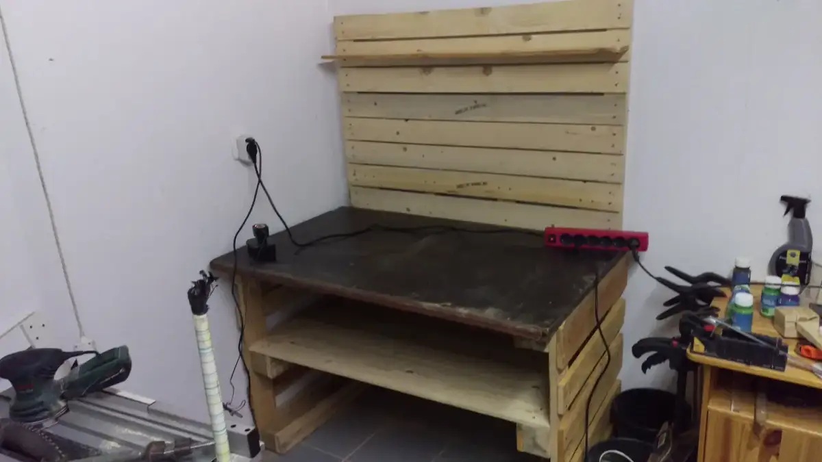 Drewniany stół warsztatowy z półkami, narzędziami i listwą zasilającą.