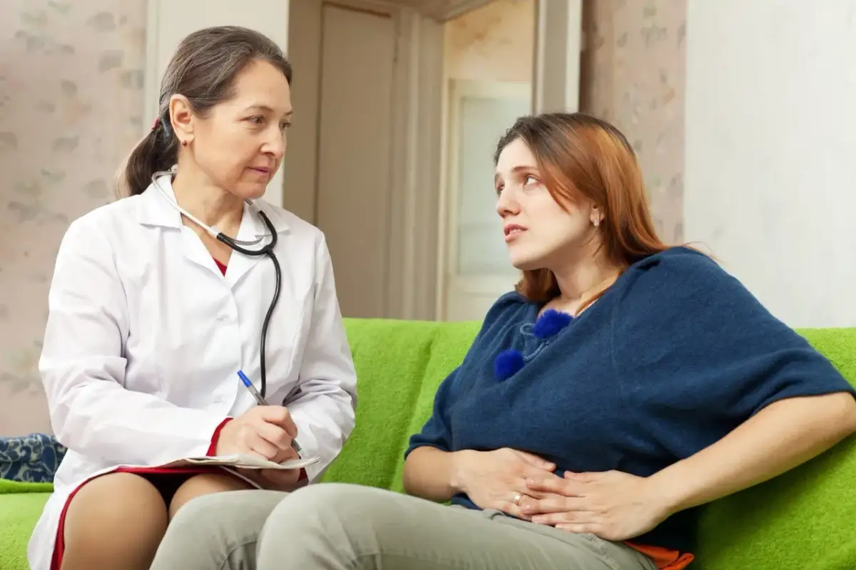 Lekarka w białym kitlu rozmawia z młodą kobietą, która trzyma się za brzuch.
