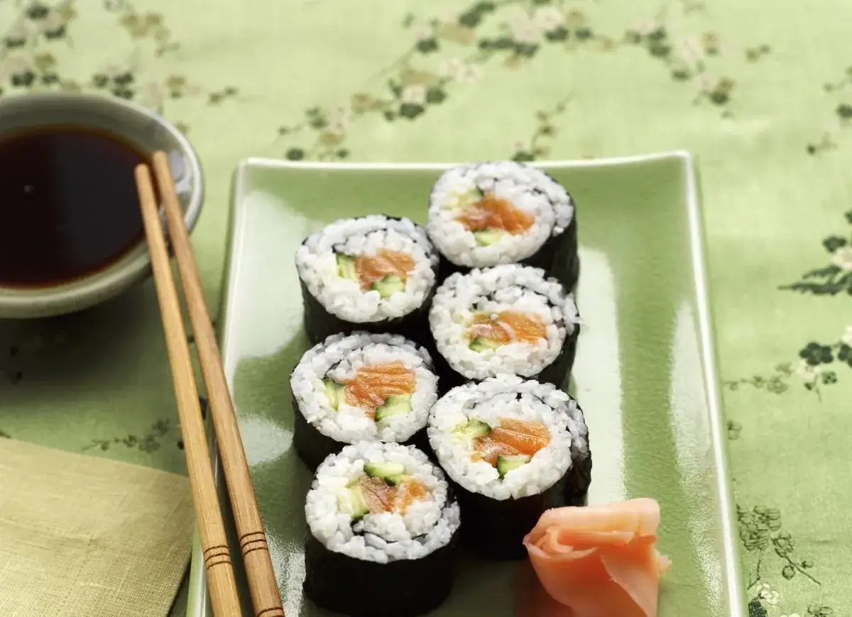 Siedem kawałków sushi z łososiem i ogórkiem na zielonym talerzu. Zastanawiasz się, ile kalorii ma sushi z łososiem?