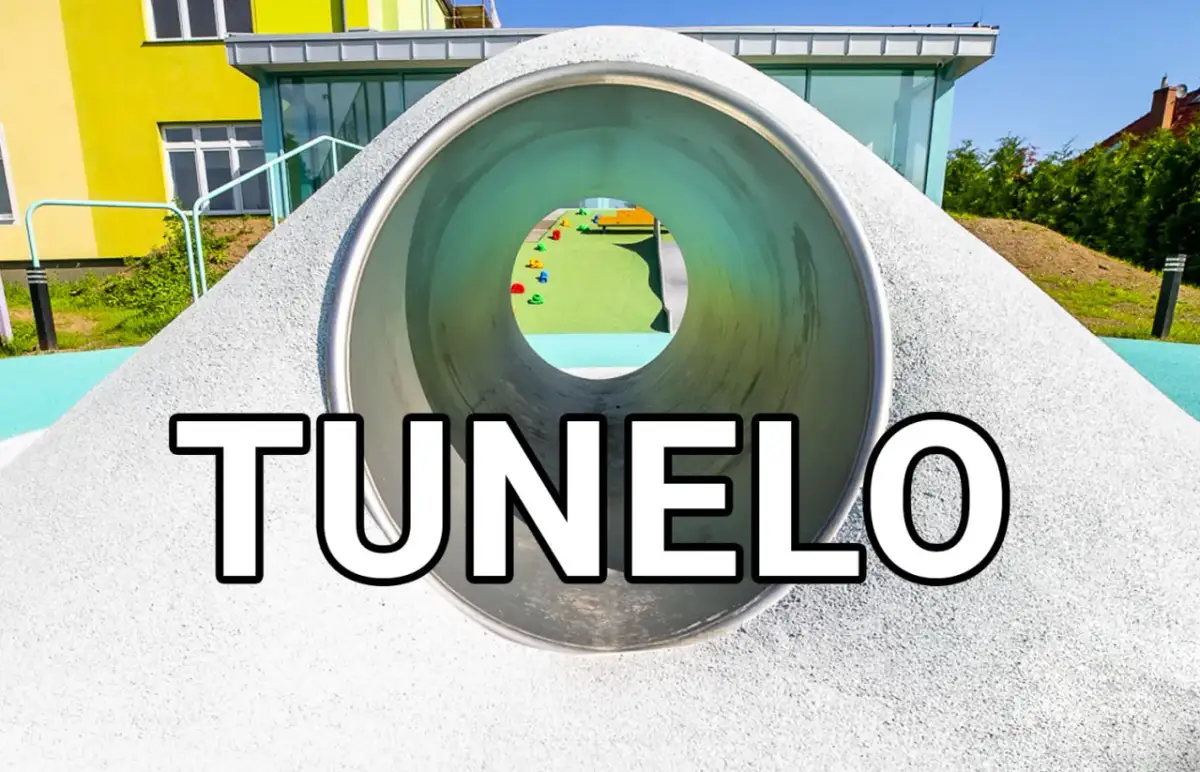 Widok przez tunel z placu zabaw na kolorowe elementy i budynek.