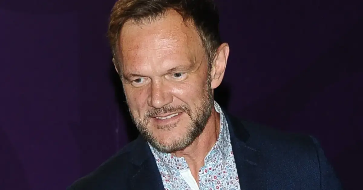 Mężczyzna z zarostem w garniturze i wzorzystej koszuli. Zastanawia się, ile zarabia aktor w filmie.