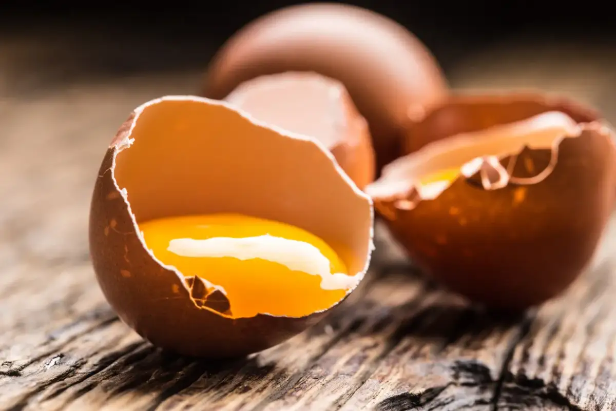 Rozbite jajko z widocznym żółtkiem na drewnianym tle.