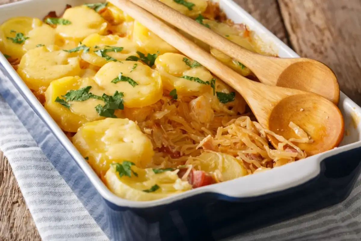 Zapiekanka z ziemniaków i kapusty w naczyniu, ozdobiona natką pietruszki, z drewnianymi łyżkami.