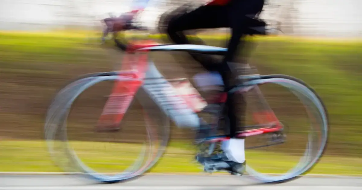 Rozmyty rowerzysta w ruchu. Pytanie: czy można jechać rowerem po alkoholu? Odpowiedź brzmi: nie.