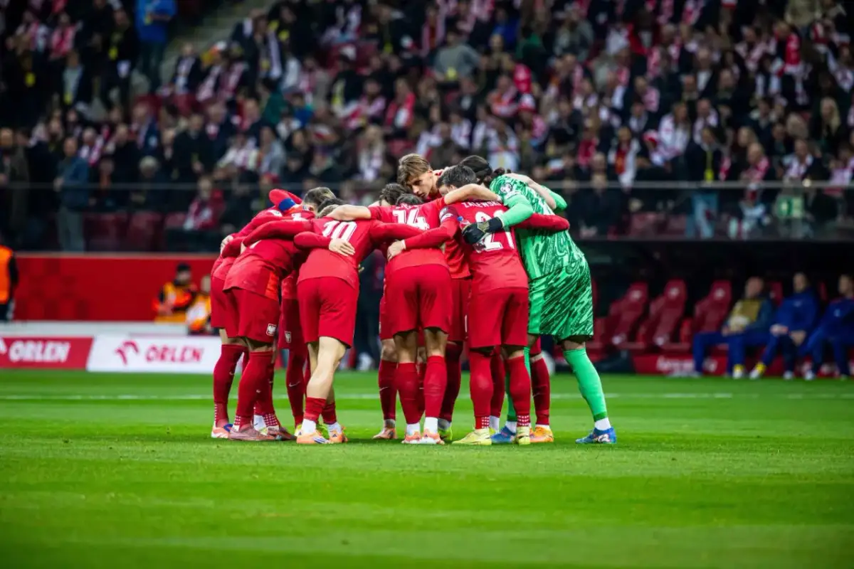 Piłkarze w czerwonych strojach tworzą zwarty krąg na murawie, wspierając się nawzajem. Czy to przed decydującym meczem o puchar narodów piłka nożna, kiedy emocje sięgają zenitu?