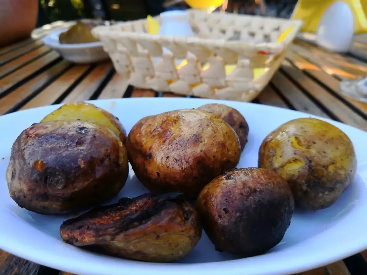 Talerz pieczonych ziemniaków na drewnianym stole, w tle koszyk i naczynia.