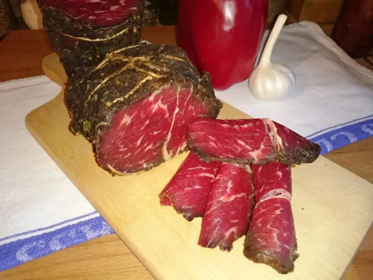 Pokrojona wołowina w paski na desce, obok papryka i czosnek. Idealna do dalszej obróbki, jak kroić wołowinę w paski.