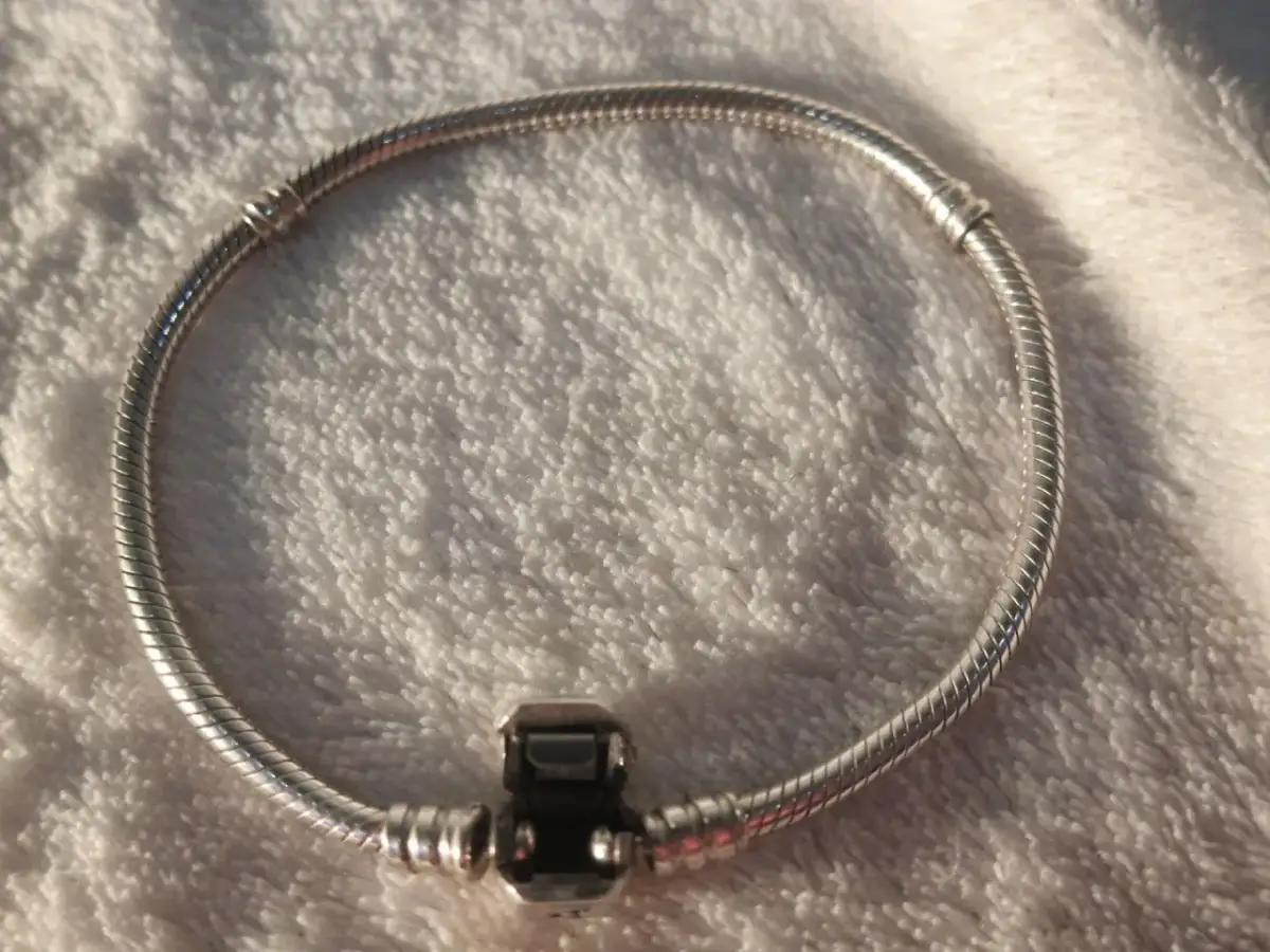 Srebrna bransoletka Pandora z zapięciem na tle białego materiału.