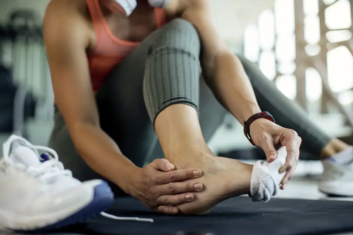 Kobieta w siłowni masuje stopę, czując mrowienie.