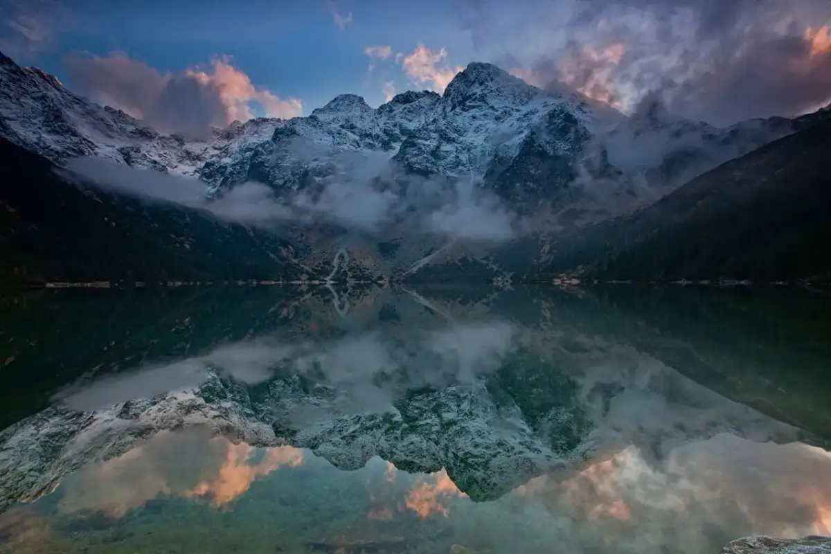 Zachód słońca nad Morskim Okiem. Chmury i ośnieżone szczyty odbijają się w tafli jeziora. Zastanawiasz się, ile kosztuje nocleg w schronisku nad Morskim Okiem?