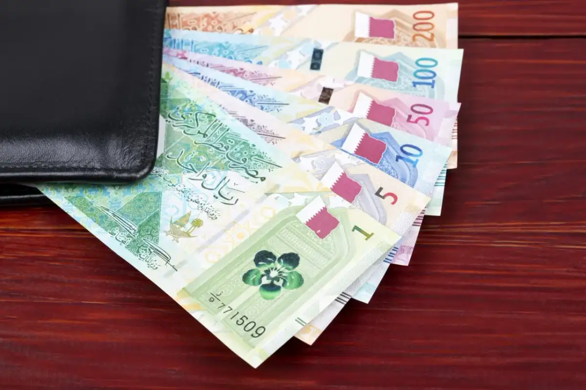 Katar jaka waluta? Na zdjęciu widać stos banknotów katarskich riali, od 1 do 200, częściowo schowanych w czarnym portfelu.