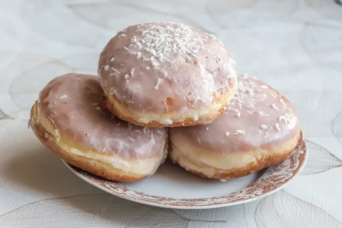 Trzy pączki z lukrem do pączków i wiórkami kokosowymi na talerzyku.