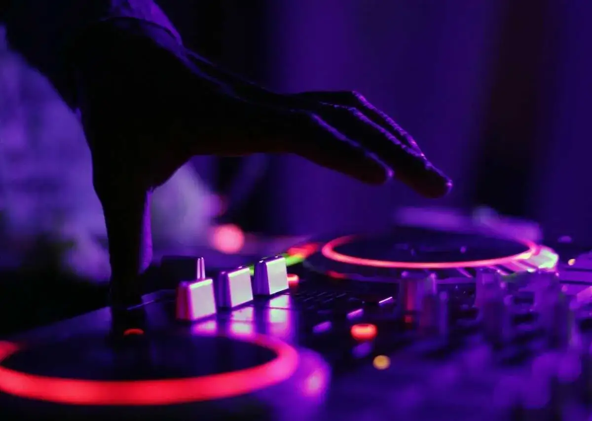 Dłoń DJ-a nad konsolą z czerwonymi i fioletowymi światłami.