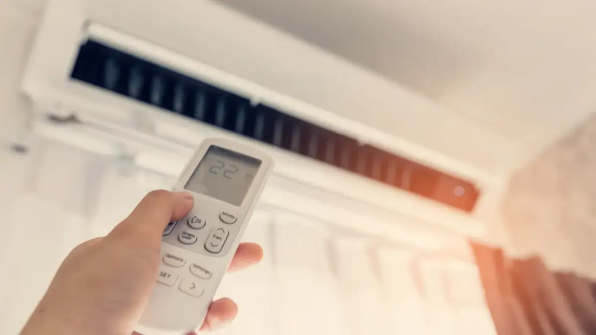 Dłoń trzymająca pilot do klimatyzacji z widoczną temperaturą 22 stopnie.