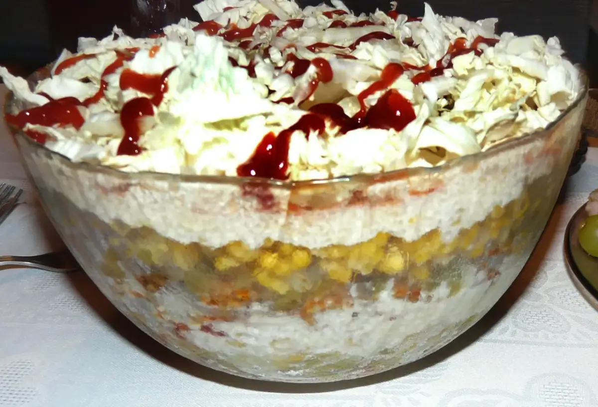 Warstwowa sałatka gyros w szklanej misie, polana ketchupem.