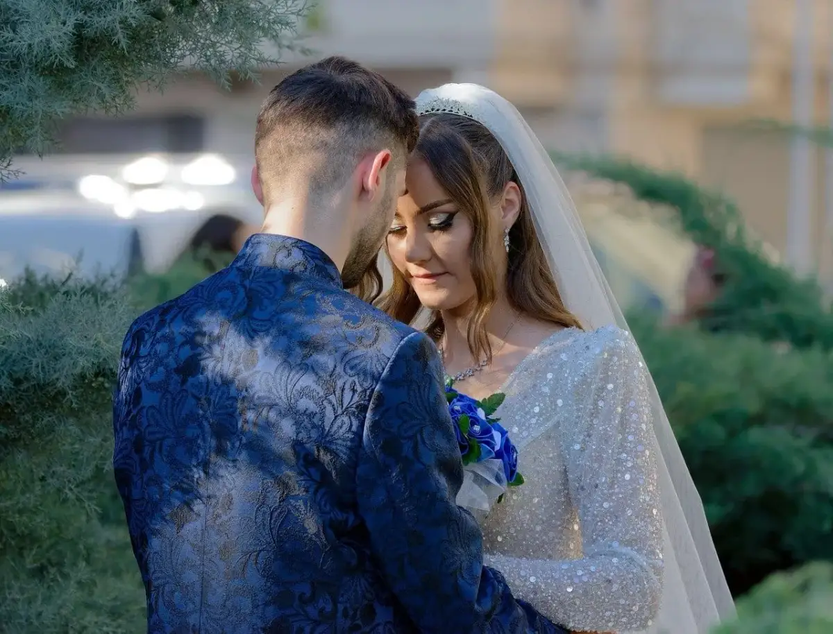 Para młoda w objęciach, panna młoda w sukni z cekinami i welonie, pan młody w granatowym garniturze.