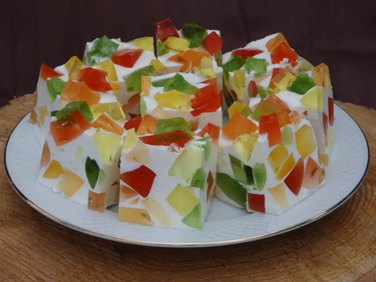 Kolorowa galaretka w białej masie, pokrojona w kostkę, na białym talerzu.