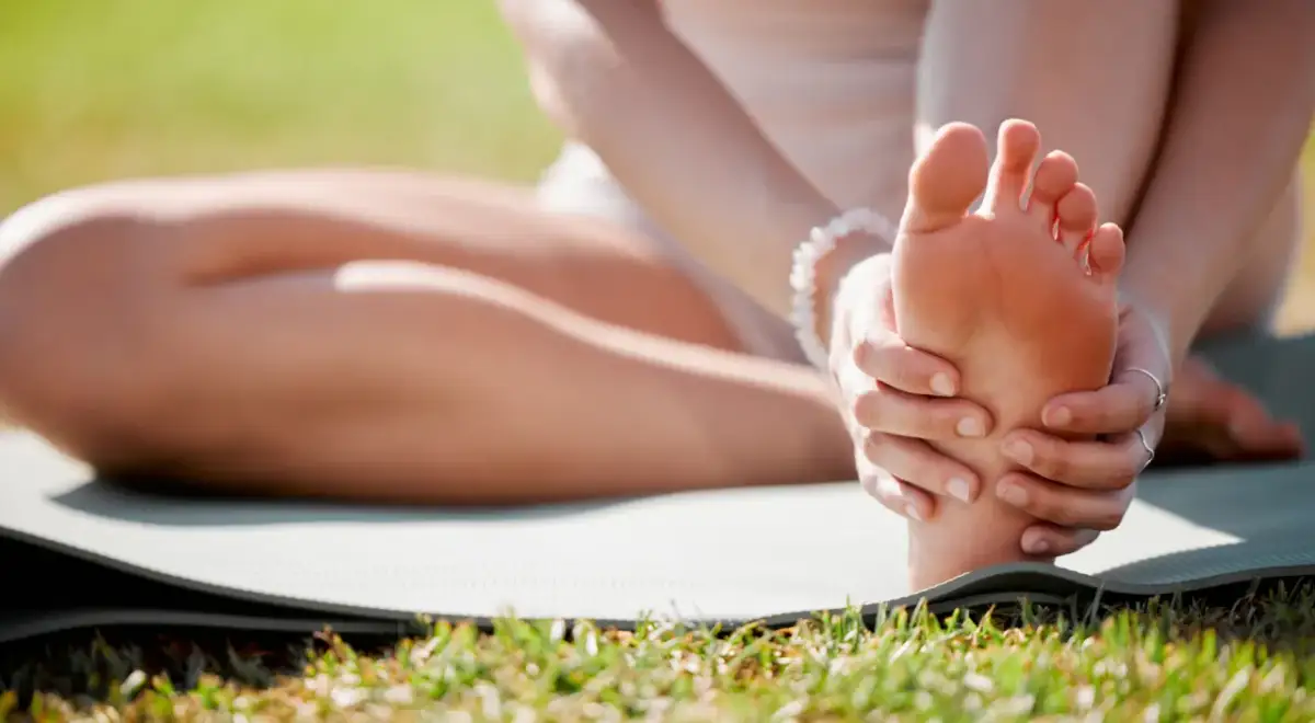 Kobieta masuje stopę na macie do ćwiczeń na trawie.