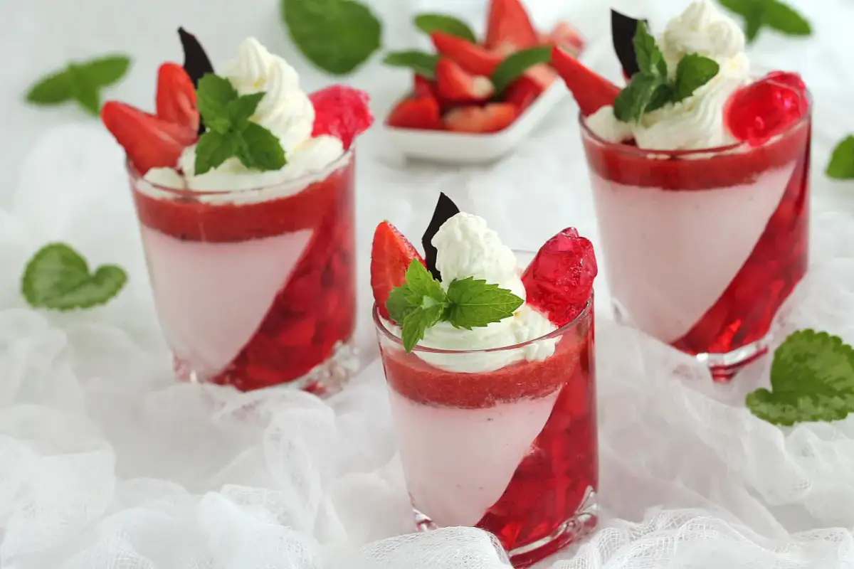 Trzy deserki z galaretką truskawkową, bitą śmietaną i miętą w szklankach.