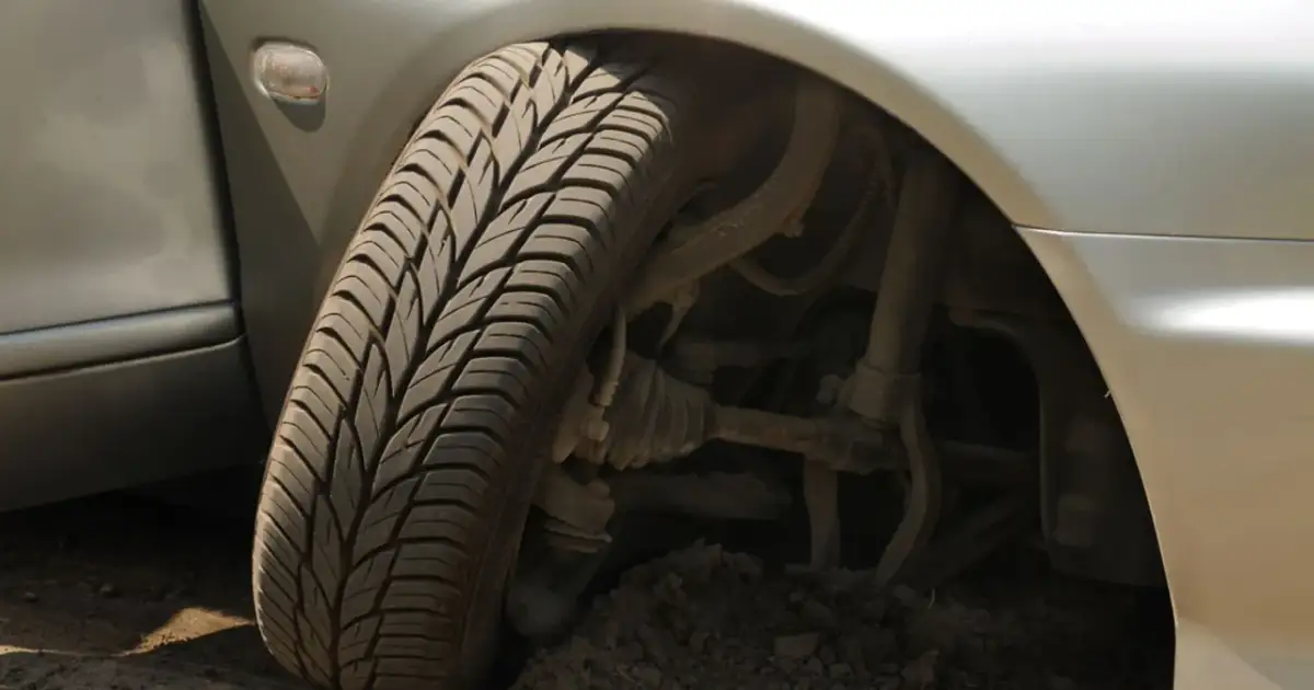 Koło samochodu osadzone w ziemi, widoczne elementy zawieszenia. Uszkodzony wahacz objawy mogą być widoczne w takim położeniu.