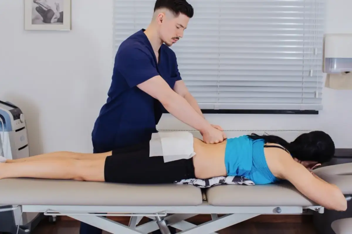 Fizjoterapeuta masuje plecy pacjentki leżącej na kozetce.