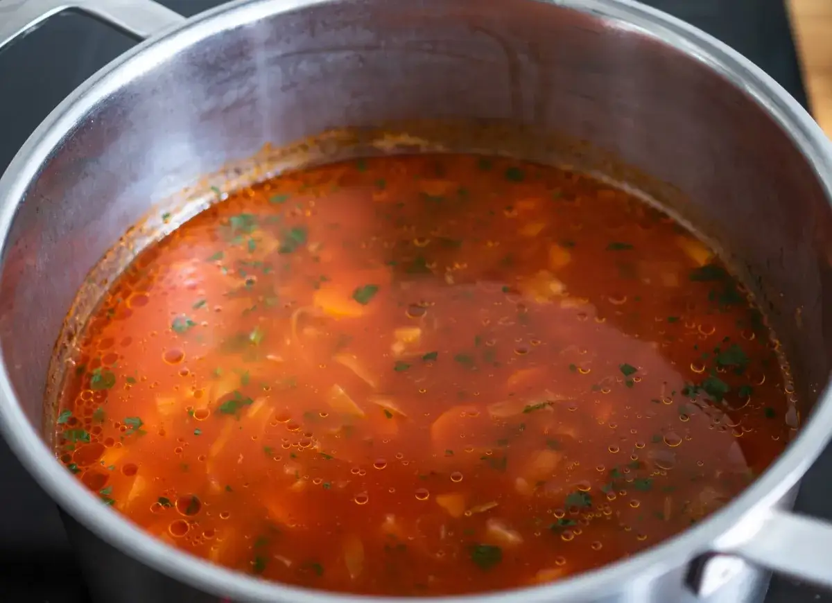 Gorąca zupa pomidorowa w garnku, z widocznymi kawałkami warzyw i zieleniną. Czy zupę pomidorową zaprawia się mąką?