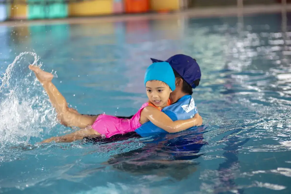 Dziecko w różowym stroju pływa z instruktorem. Dowiedz się, ile kosztuje nauka pływania dla dzieci.