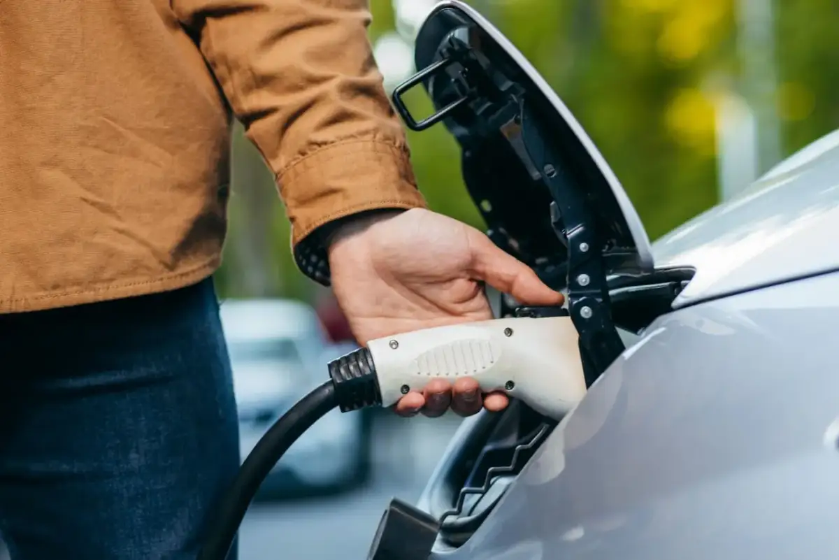 Ręka podłącza ładowarkę do samochodu elektrycznego. Prosty sposób, jak otworzyć stację ładowania samochodów elektrycznych.