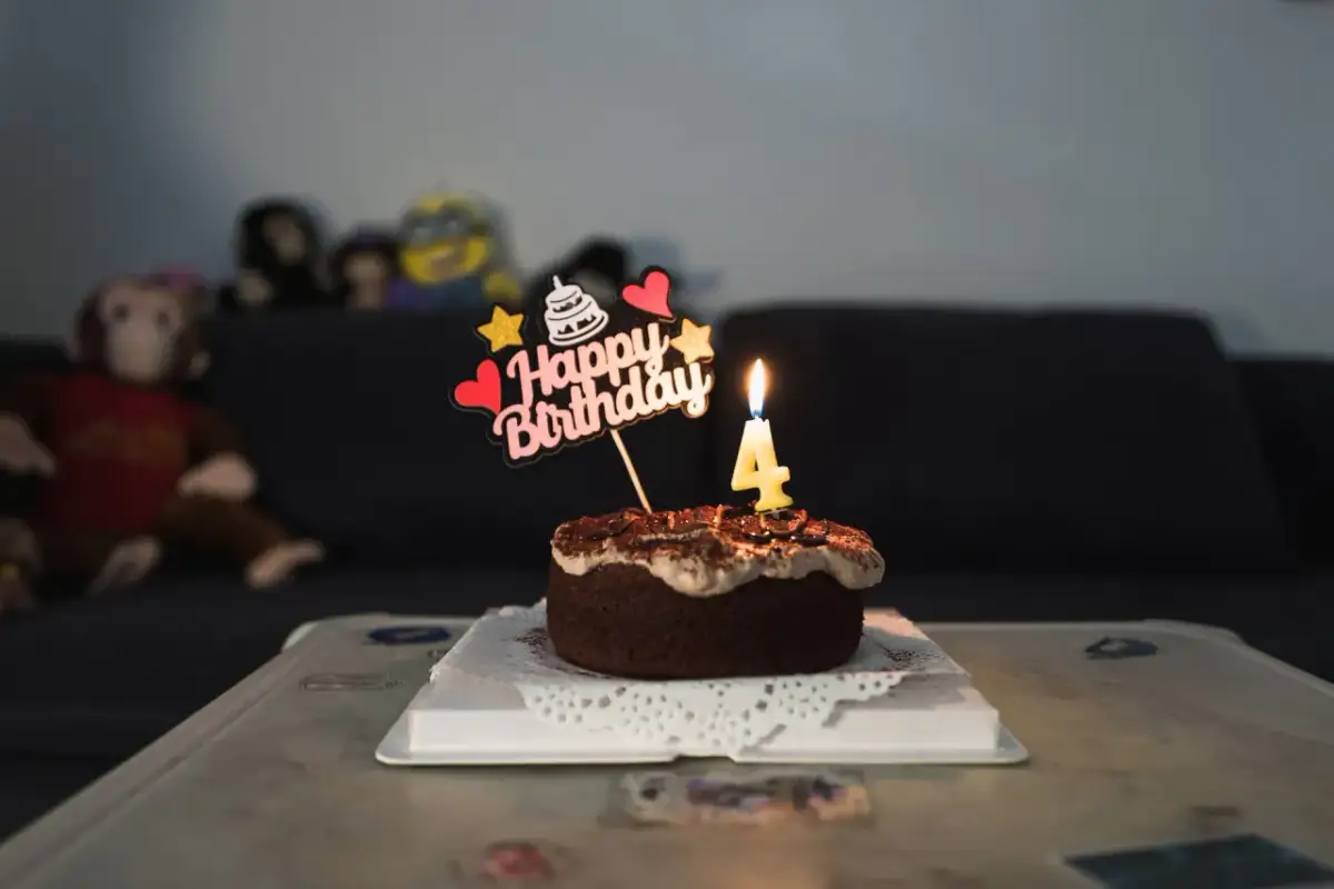 Mały tort czekoladowy z napisem "Happy Birthday" i świeczką w kształcie cyfry 4.