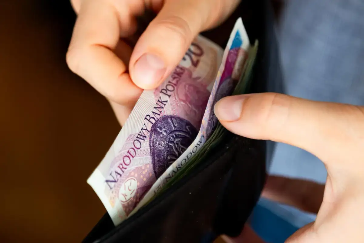 Dłonie wkładają polskie banknoty do czarnego portfela.