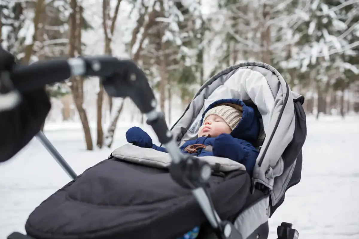Śpiące dziecko w wózku, ubrane w ciepły kombinezon zimowy, czeka na spacer.