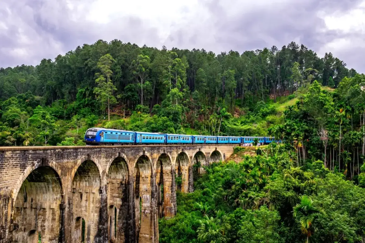 Niebieski pociąg przemierza dziewięciookopowy most kolejowy w otoczeniu bujnej zieleni. Podróżując po Sri Lance, można poczuć się bezpiecznie, podziwiając takie widoki.