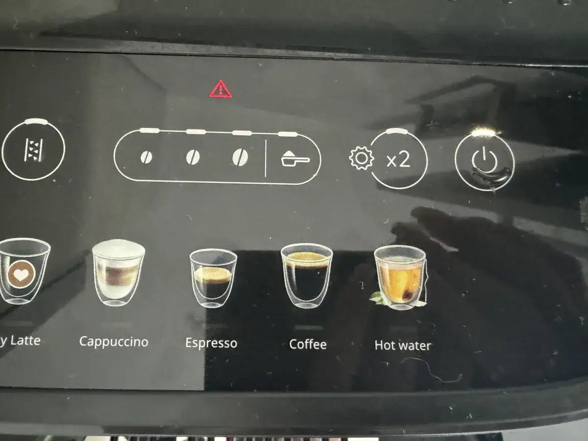 Ekspres DeLonghi z czerwoną kontrolką ostrzegawczą. Widoczne ikony napojów: latte, cappuccino, espresso, kawa, gorąca woda.