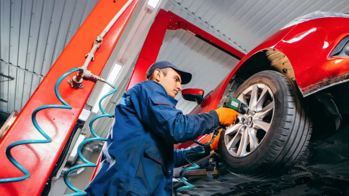 Mechaniker wechselt Reifen an einem roten Auto mit einem Schlagschrauber.