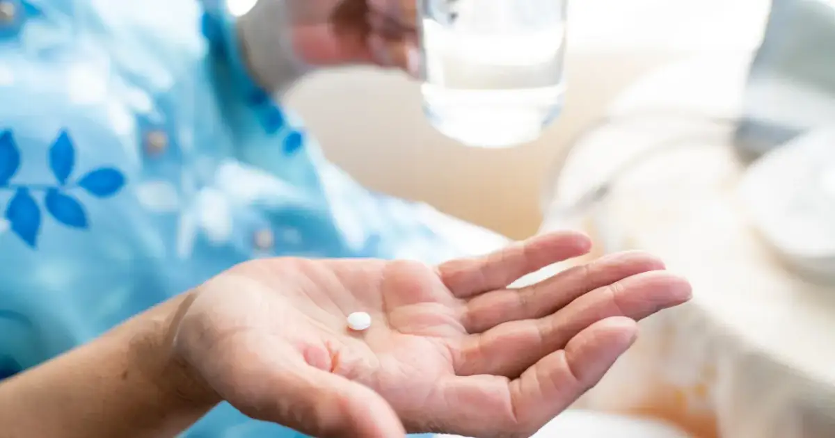 Dłoń trzyma białą tabletkę, przygotowując się do połknięcia. Zrozumienie aspiryna działanie to klucz do ulgi w bólu.