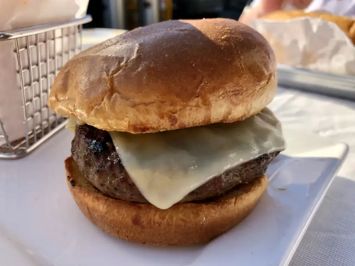 Hamburger z serem na białym talerzu, obok koszyka na frytki.