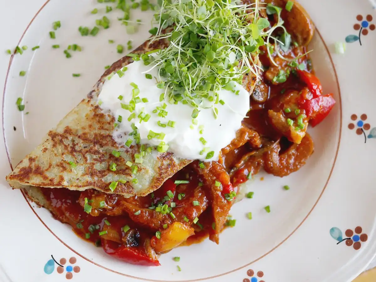 Placki ziemniaczane z gulaszem, śmietaną i kiełkami na talerzu.